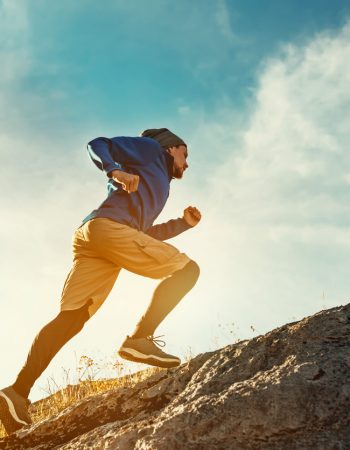 Skyrunner athlete runs uphill against sunset or sunrise sky and sun. Skyrunning concept